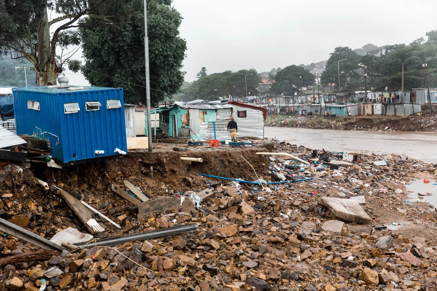 Blue container building teetering on the edge of a washed-away river.